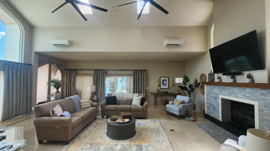 Luxurious living room with cozy sofas, two mini-split air conditioners, and a wide TV mounted above the fireplace
